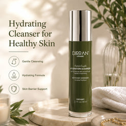 A bottle of DIRRAN ORGANIC Hydrating Cleanser stands on a marble tray in a styled bathroom setting with a towel, glass vase, and leaves. Text on the left reads 'Hydrating Cleanser for Healthy Skin' with three feature icons.